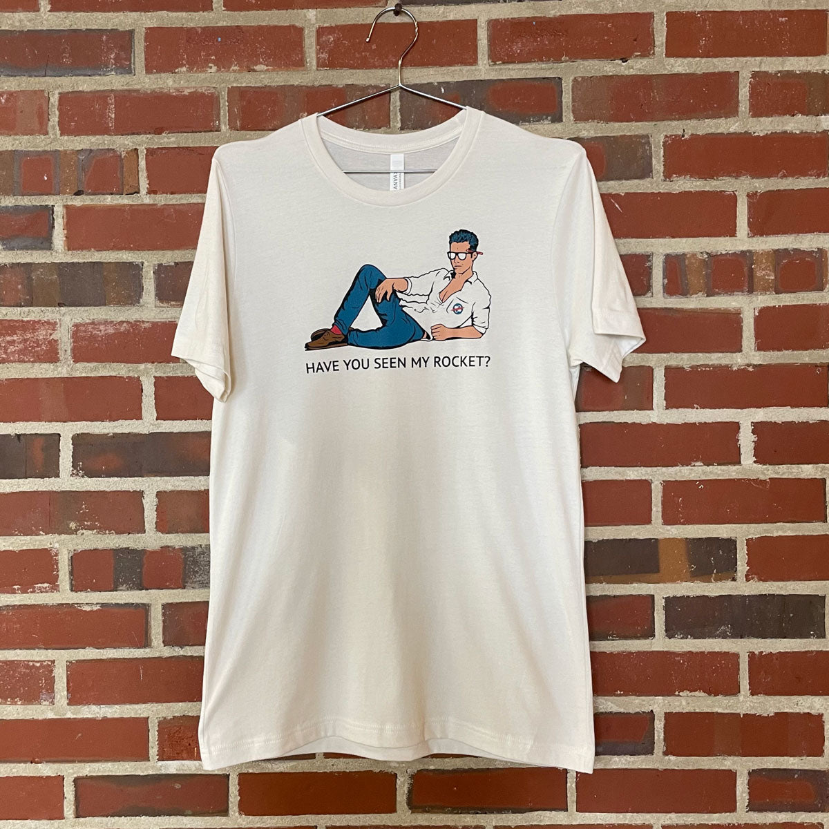 Image of scientist lounging with text "Have you seen my rocket?" on white shirt hanging against brick wall at Lowe Mill