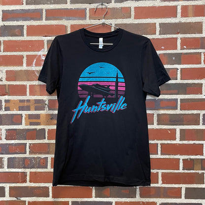 Pathfinder rocket and Saturn V silhouetted against a pink and blue sunrise with "huntsville" text on a black t-shirt against a red brick wall