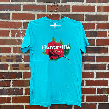 Image of red camellia flower with text "Huntsville Alabama" on teal t-shirt hanging against brick wall in Lowe Mill