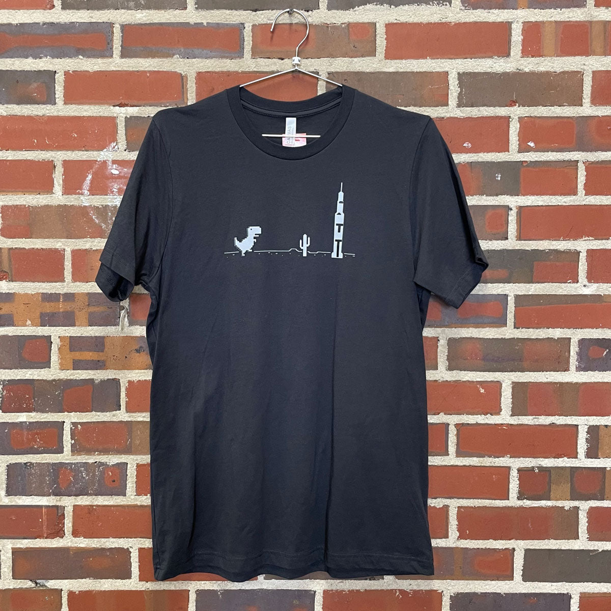 Internet dinosaur from a classic no internet game with the Saturn V rocket design on a T-Shirt against a brick wall