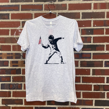 Image of astronaut preparing to throw American flag on light heather grey shirt hanging against brick wall at Lowe Mill