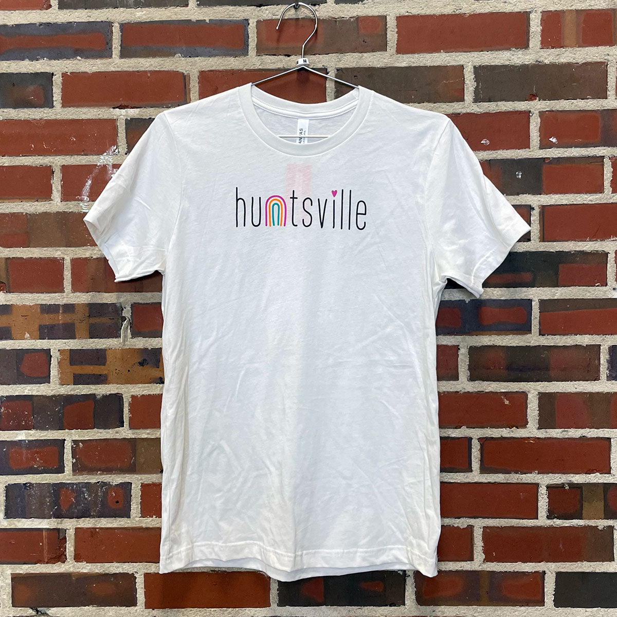 the text "huntsville" with a rainbow as the n design on a t-shirt against a red brick wall