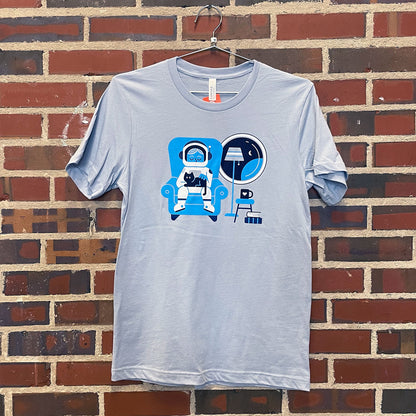 Image of astronaut cozy at home with kitty on blue shirt hanging against brick wall at Lowe Mill