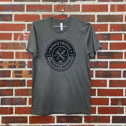 T-Shirt with the design of a seal with the text "armstrong rocket repair" on a red brick wall