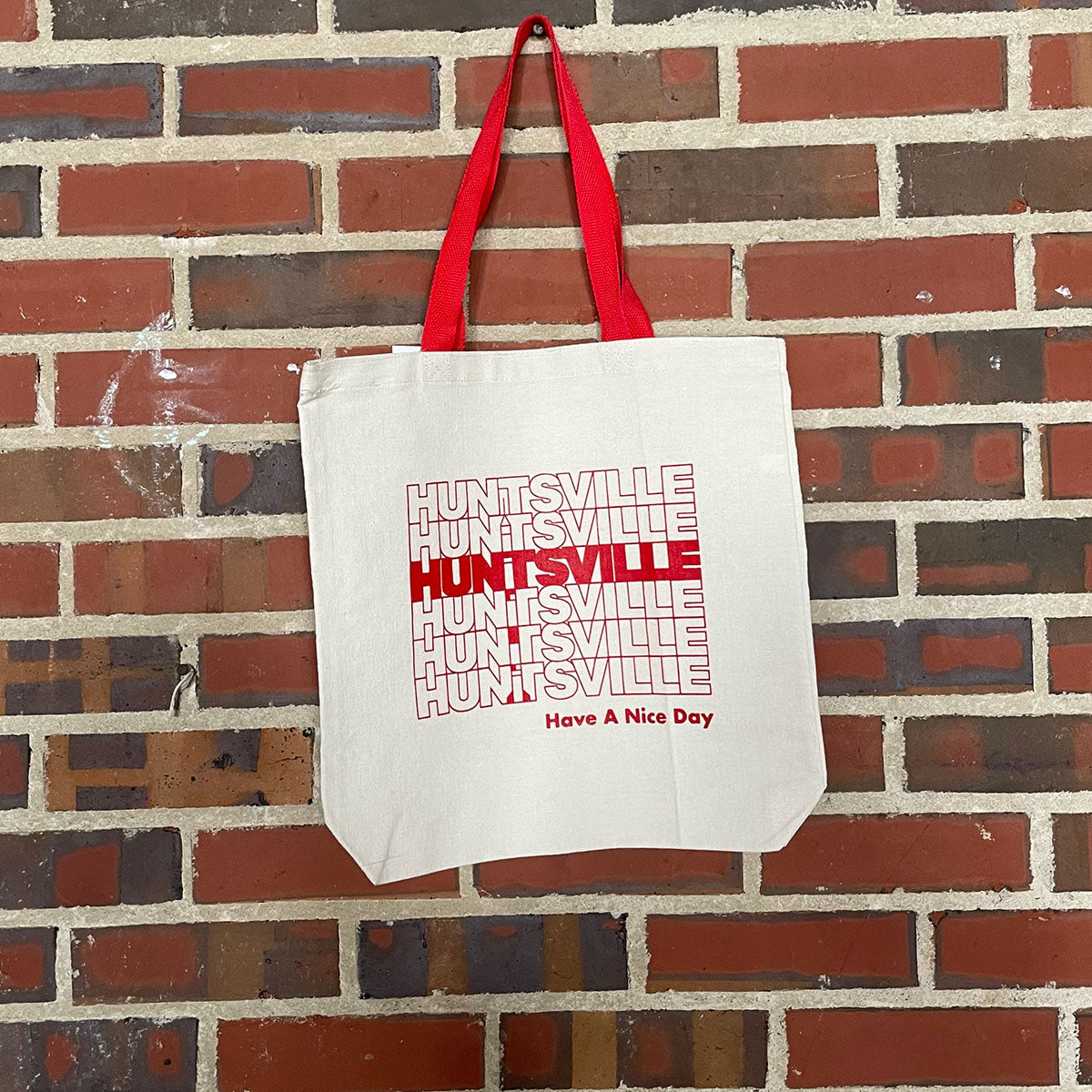 Image of red text "Huntsville Have a Nice Day" on natural tote hanging against brick wall at Lowe Mill